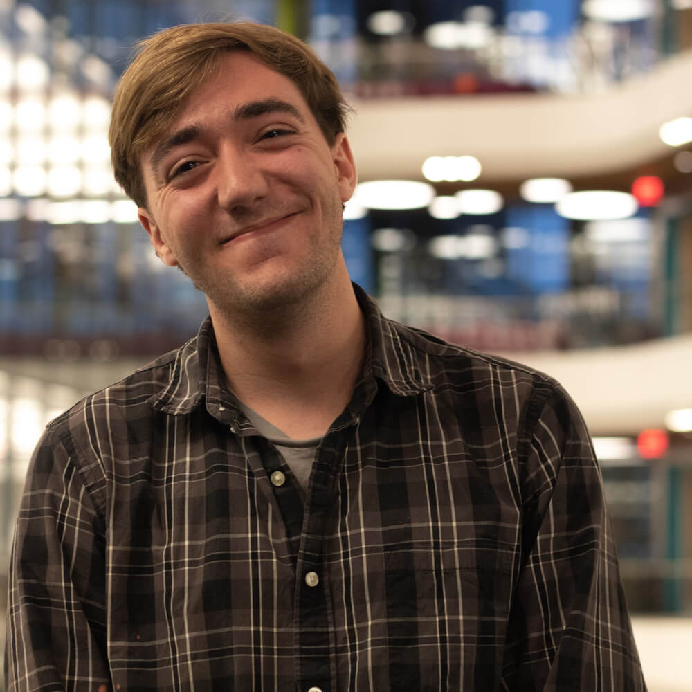 A picture of Benjamin Roy Greenvall. He is posing for the camera and smiling. He is wearing a brown plaid shirt. 