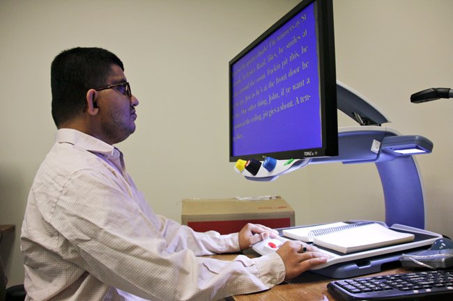 A man in a collared shirt looking at a big computer monitor on his desk.