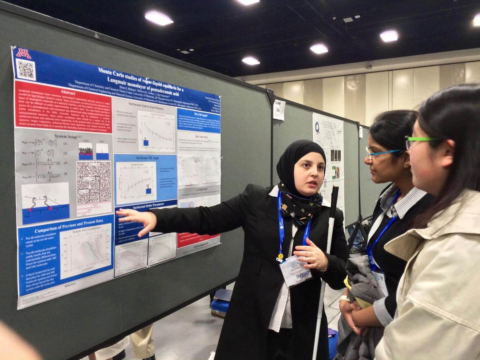Mona Minkara presents a poster of her research to two fellow chemists. 