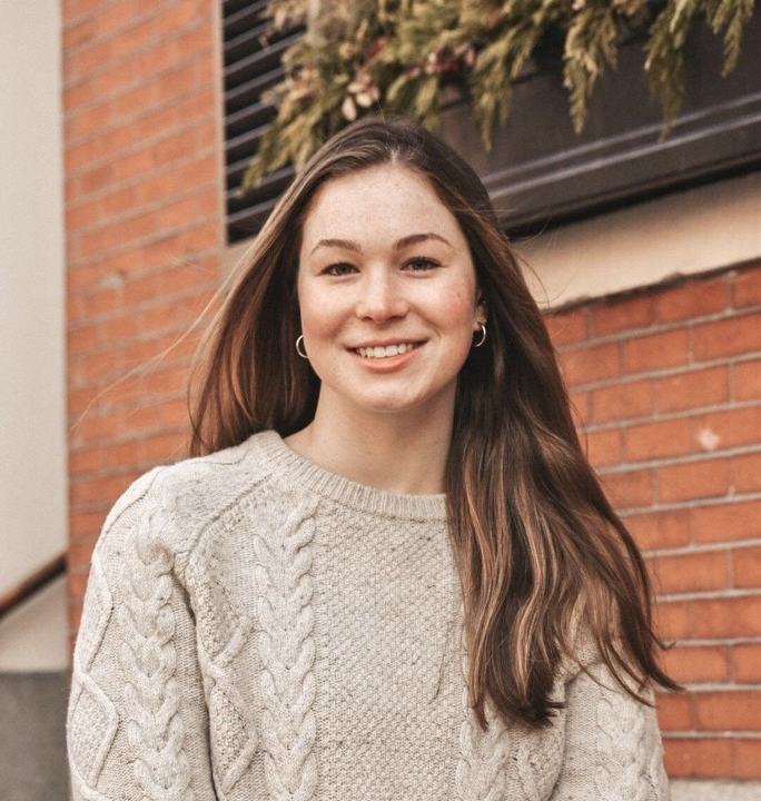 A photo of Anne Sigl posing on camera. She is wearing a beige sweater.